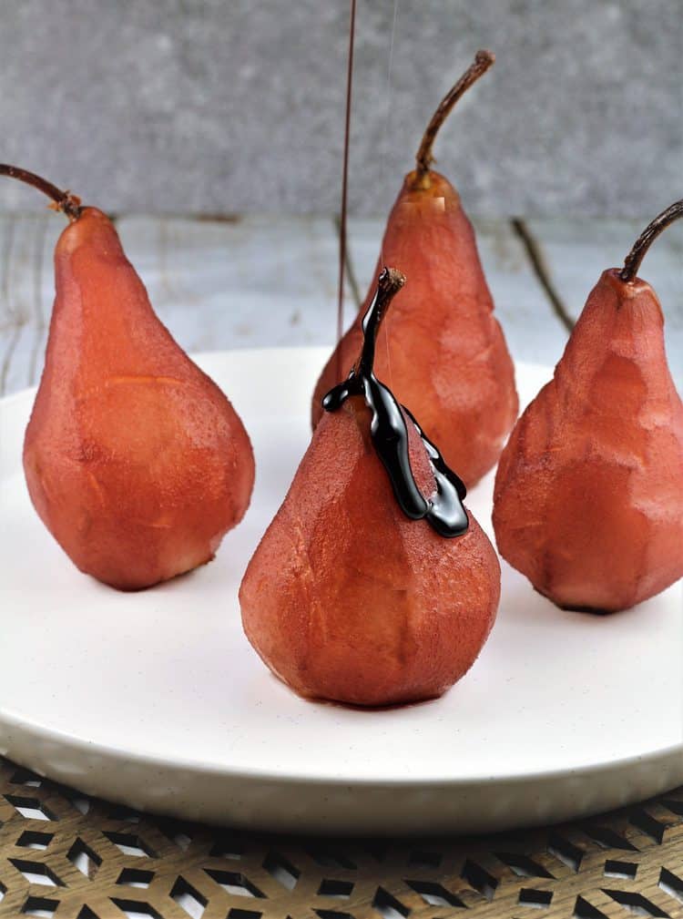 4 poached pears on serving plate with syrup drizzled on one of them