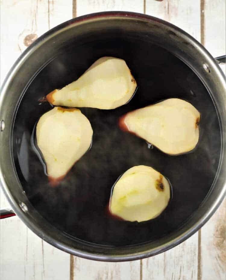 Whole Bosc pears in red wine in saucepan for poaching.