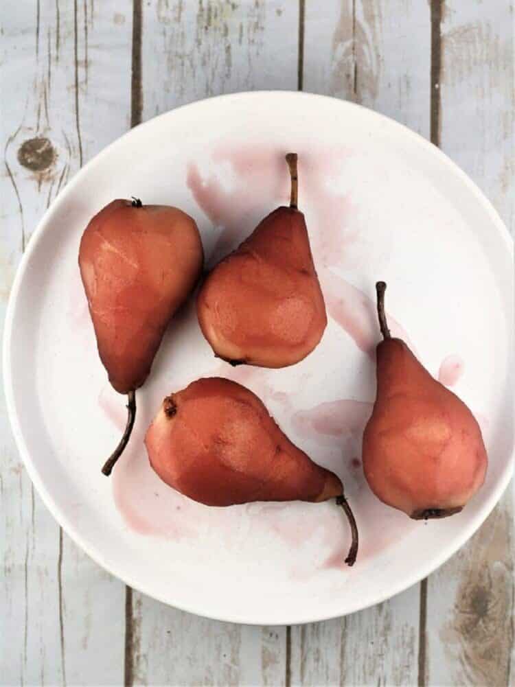Red wine poached pears resting on plate.