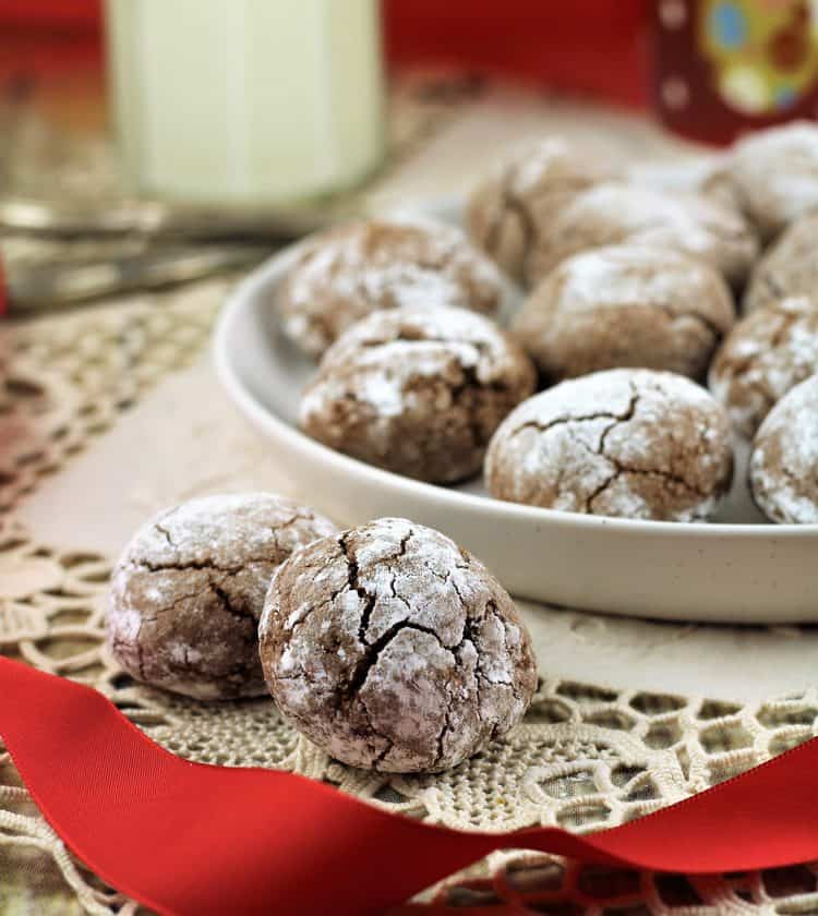 2 Chocolate Espresso Amaretti Cookies on side of plate full of cookies and milk glass in background