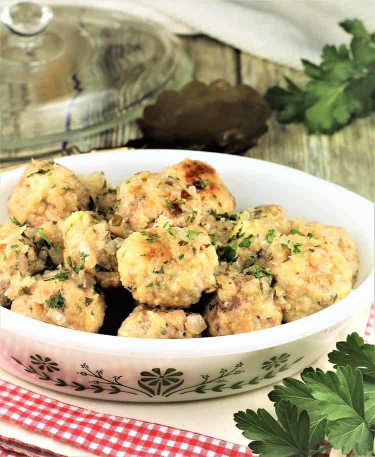 meatballs in white glass casserole dish with parsley sprig in foreground and lid in background