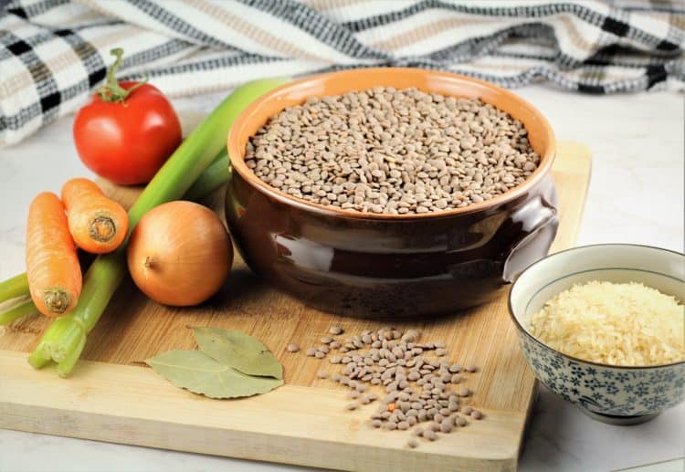 ceramic bowl of brown lentils on wood board with carrots, celery, onion and bowl of rice