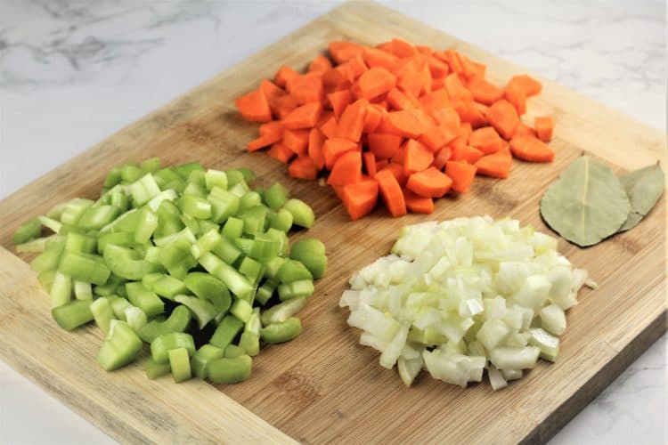 wood board with diced carrots, celery, onion and bay leaves