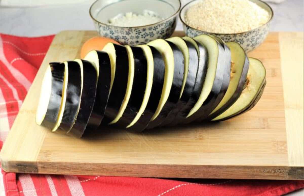Sliced eggplant into rounds on wood board.