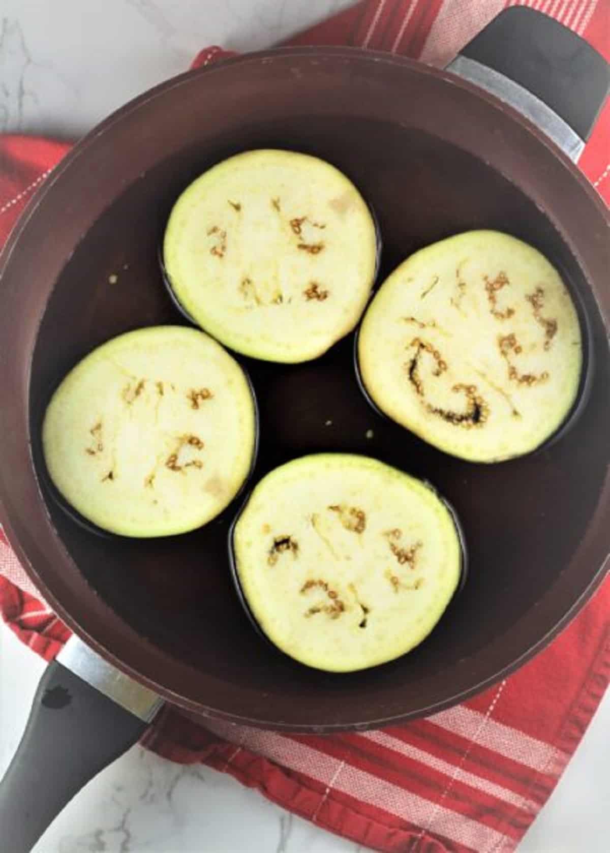 Eggplant slices in skillet with water.
