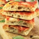 No knead pizza Margherita squares piled on one another on wood serving board
