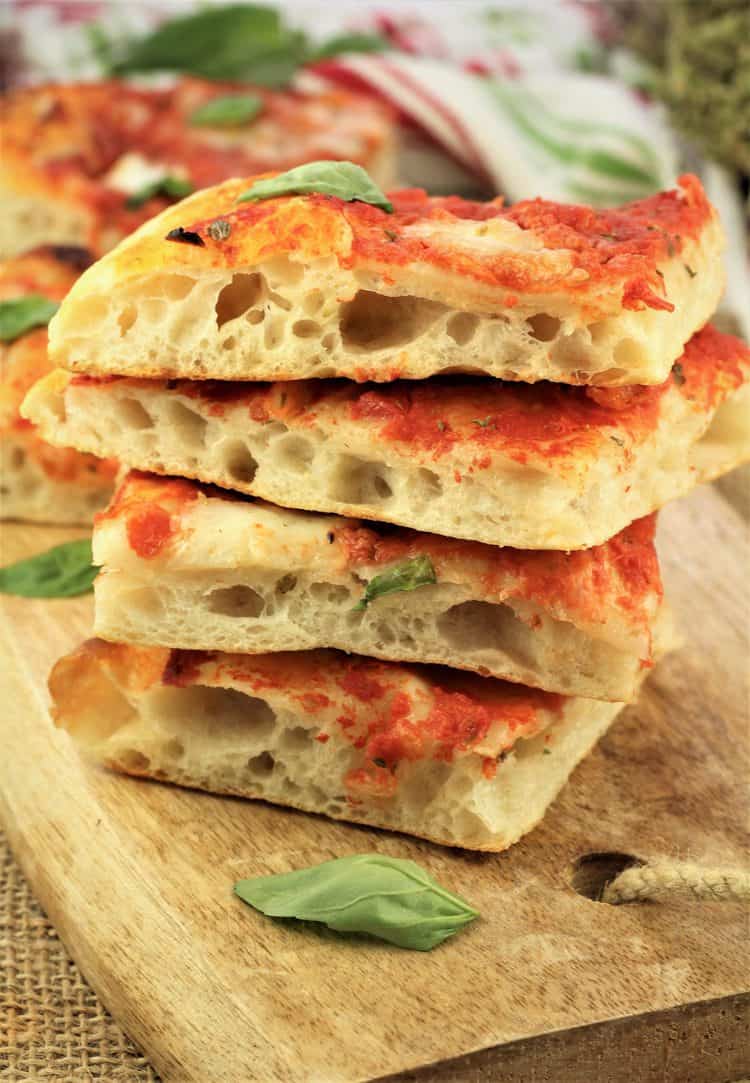 No knead pizza Margherita squares piled on one another on wood serving board