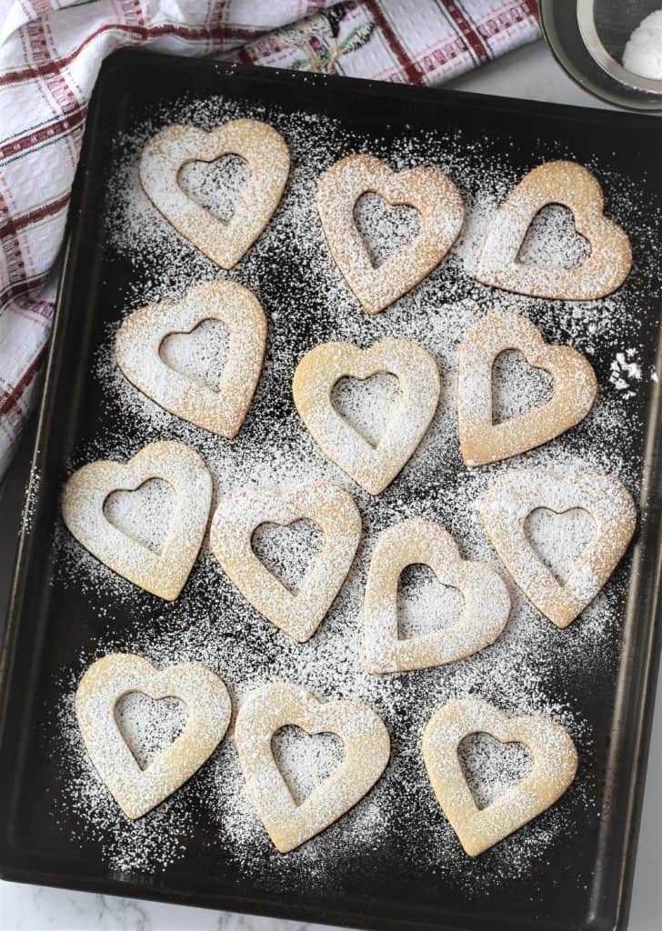 cookie hearts dusted in powdered sugar on baking sheet 