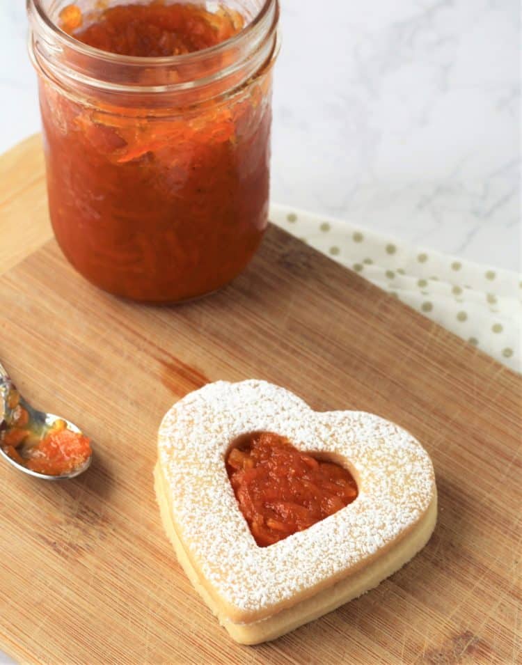 heart cookie filled with jam next to jam jar and spoon