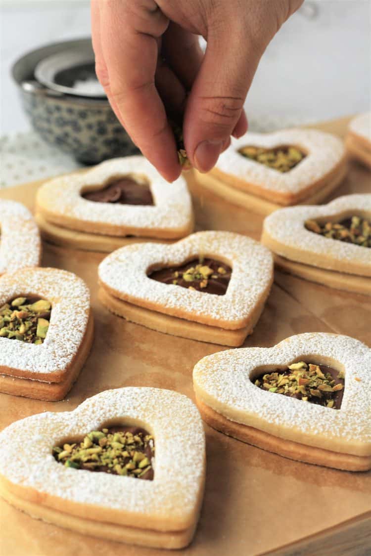 sprinkling toasted pistachios on Nutella filled cookie hearts 