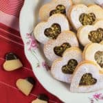 heart shaped cookies with Nutella filling on plate with small heart cutouts dipped in chocolate on the side