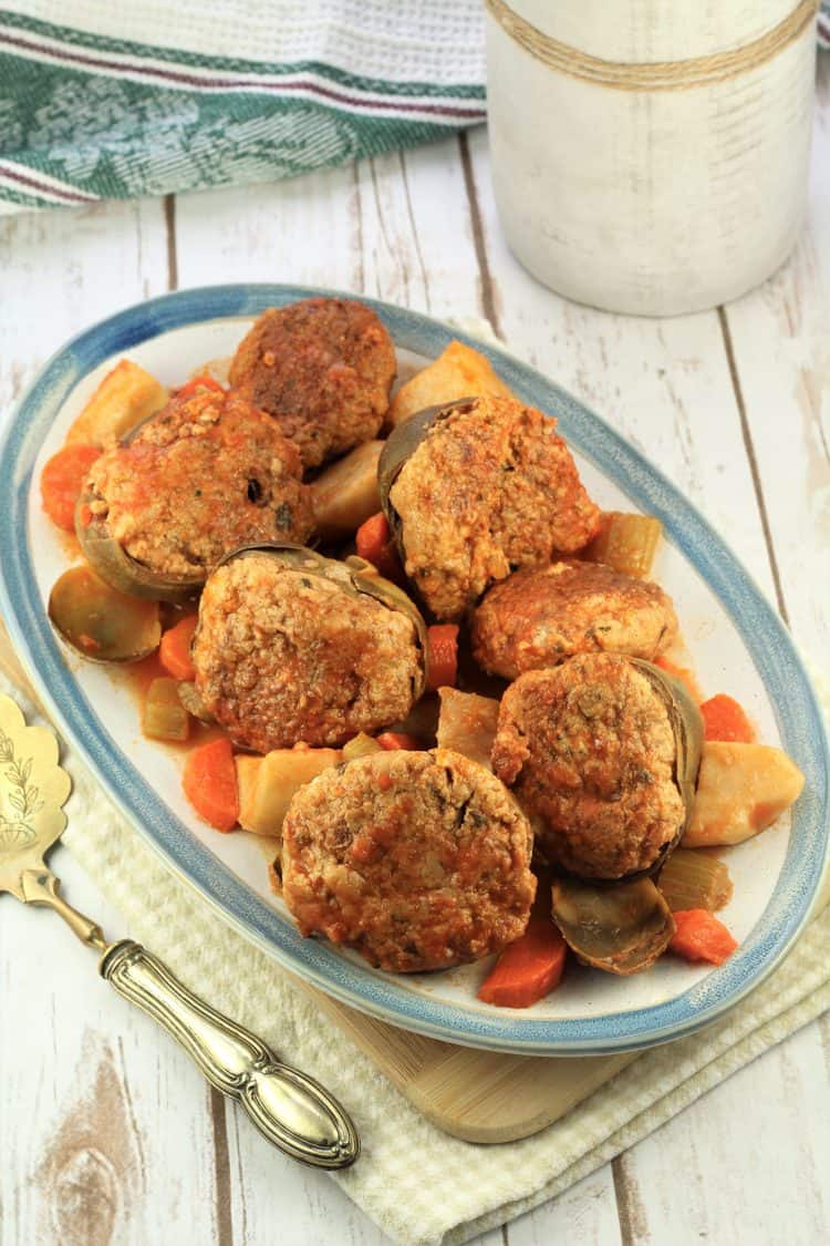 blue rimmed serving plate filled with stewed stuffed artichokes and vegetables