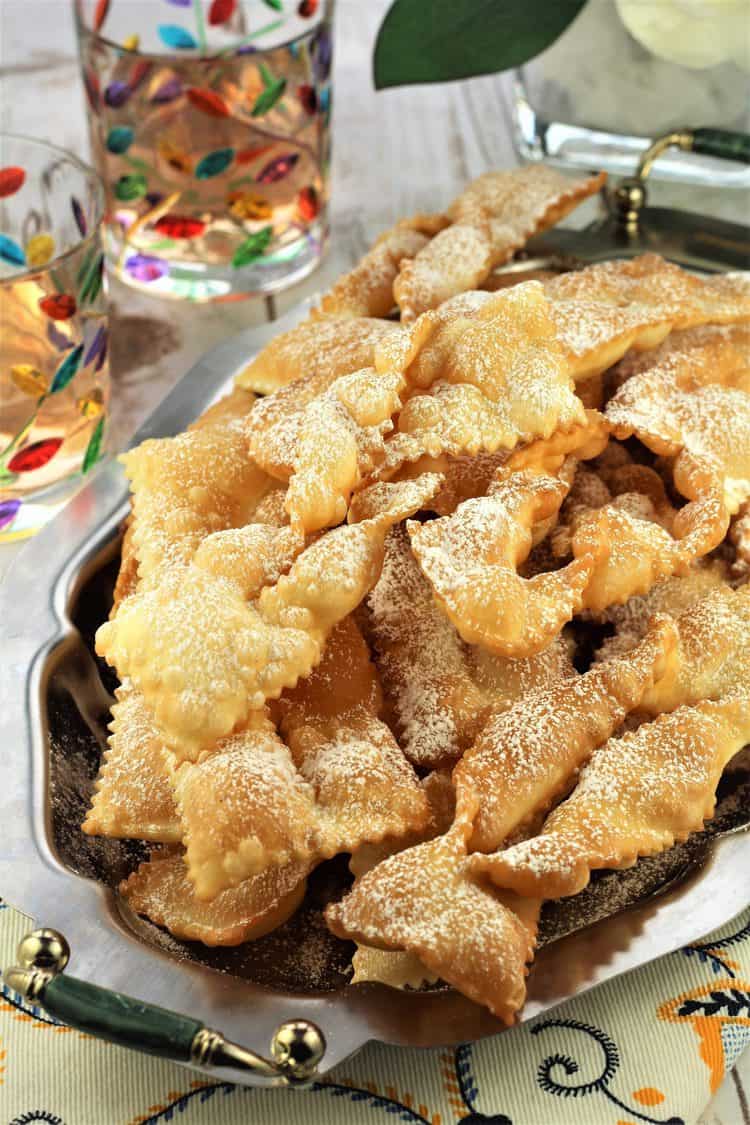 silver tray piled with chiacchiere with 2 colorful goblets on the side