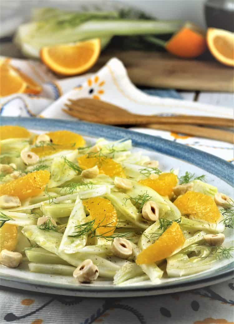 blue rimmed white plate topped with sliced fennel and orange salad with hazelnuts