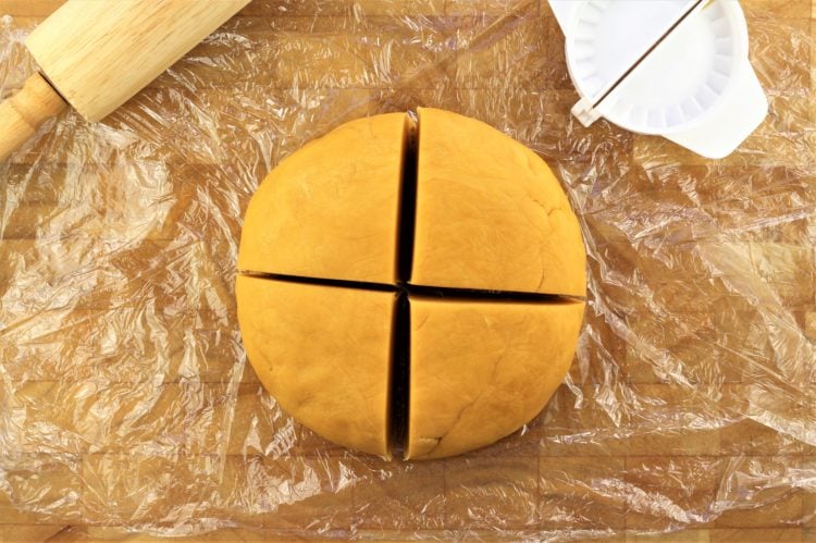 round chickpea flour dough divided into 4 pieces with rolling pin and empanada cutter on side