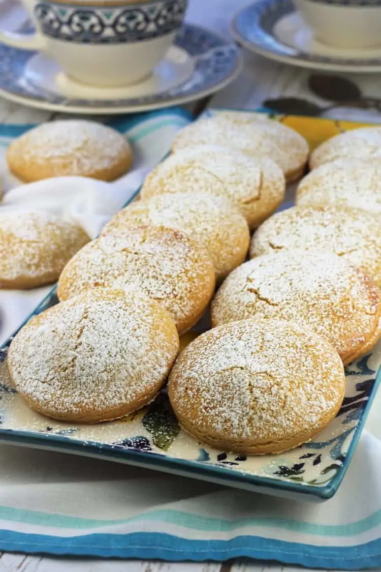rectangular plat filled with round cookies dusted in powdered sugar with coffee cup behind it