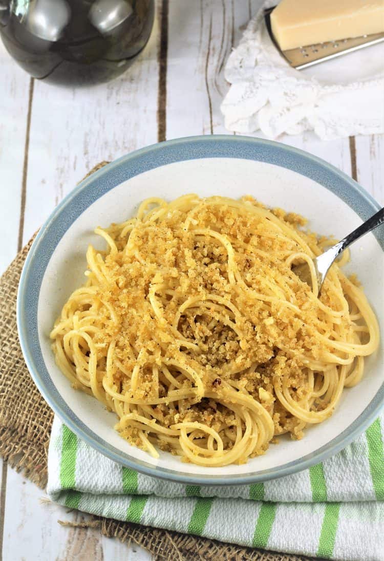 blue rimmed white bowl filled with spaghetti with breadcrumbs and fork inserted in it 
