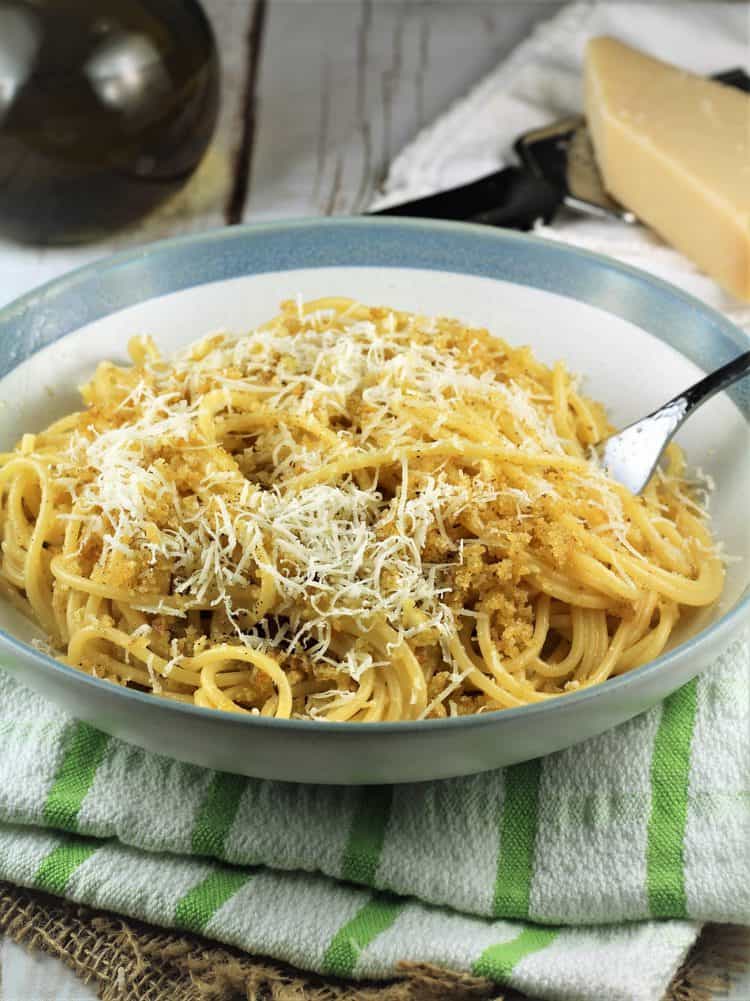 blue rimmed white bowl filled with spaghetti with breadcrumbs topped with cheese