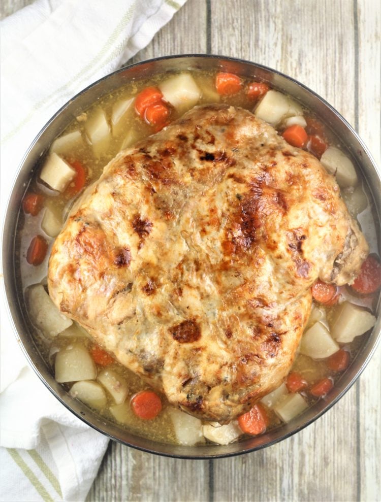 roast stuffed chicken in round baking pan with potatoes and carrots around it