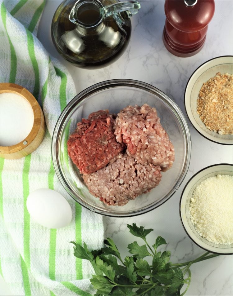 ingredients for meatballs in individual bowls with egg, parsley, olive oil and pepper mill