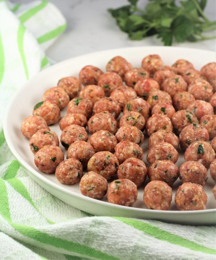 tiny raw meatballs on round plate with parsley in background