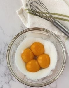 4 egg yolks with sugar in glass bowl with whisk on side