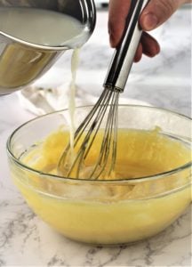 tempering eggs with warm milk poured into bowl while being whisked