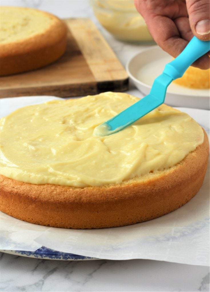 blue offset spatula spreading pastry cream on sponge cake