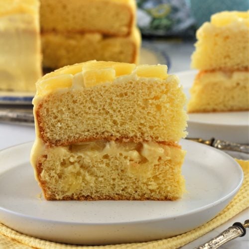 slice of pineapple cake with pastry cream on plate with cake behind it