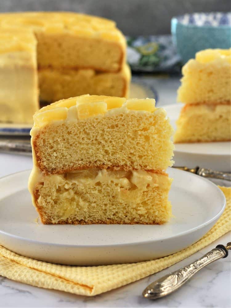 slice of pineapple layer cake with pastry cream on plate with remaining cake in background