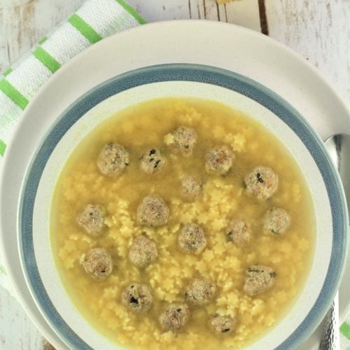 bowl of pastina soup with tiny meatballs with cheese in background