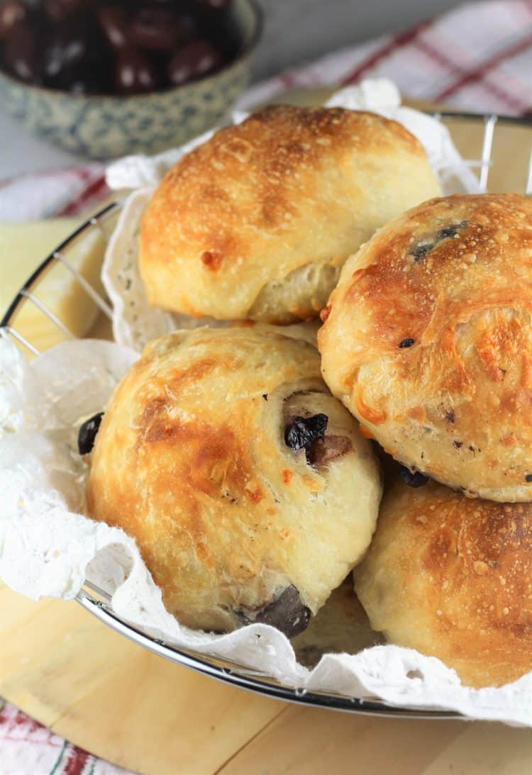 olive and cheese buns in breadbasket on wood board with bowl of olives