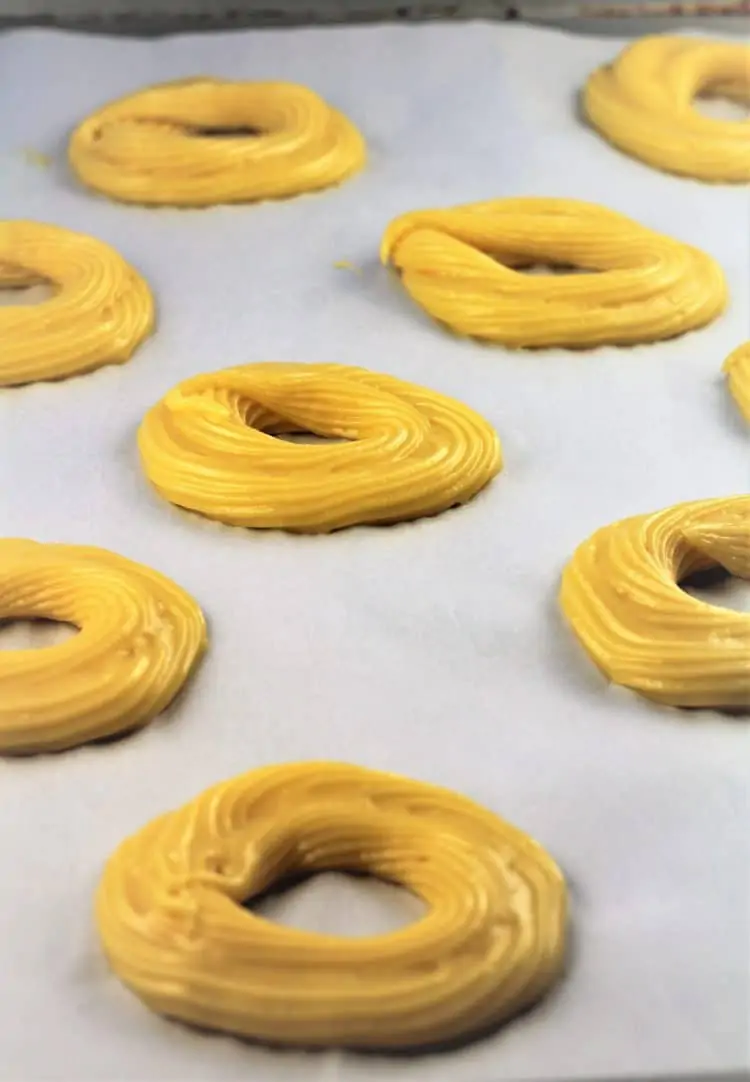 piping choux pastry into rings onto baking sheet