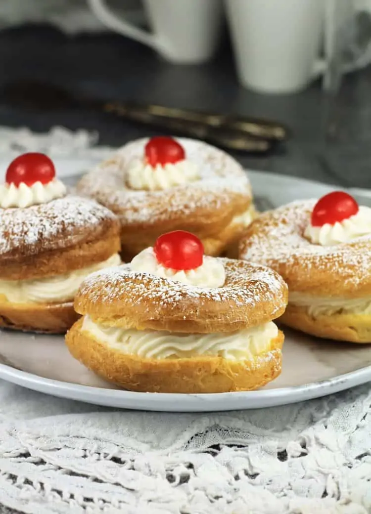 4 cherry topped zeppole with ricotta filling for St-Joseph's Day on white plate with cups in background