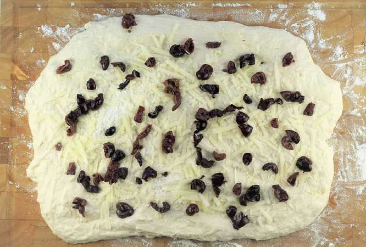 No knead dough flattened into a rectangular and topped with chopped olives and shredded cheese.