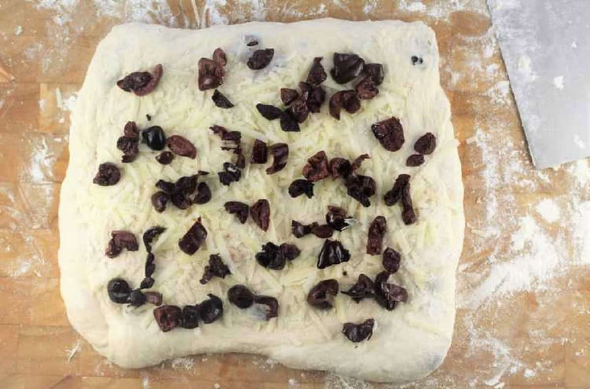 No knead pizza dough topped wih chopped olives and shredded cheese.