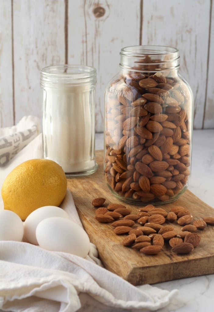 mason jar filled with almonds, jar with sugar, eggs and lemon on wood board