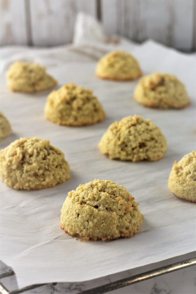 mounds of baked almond cookies on parchment paper covered wire rack