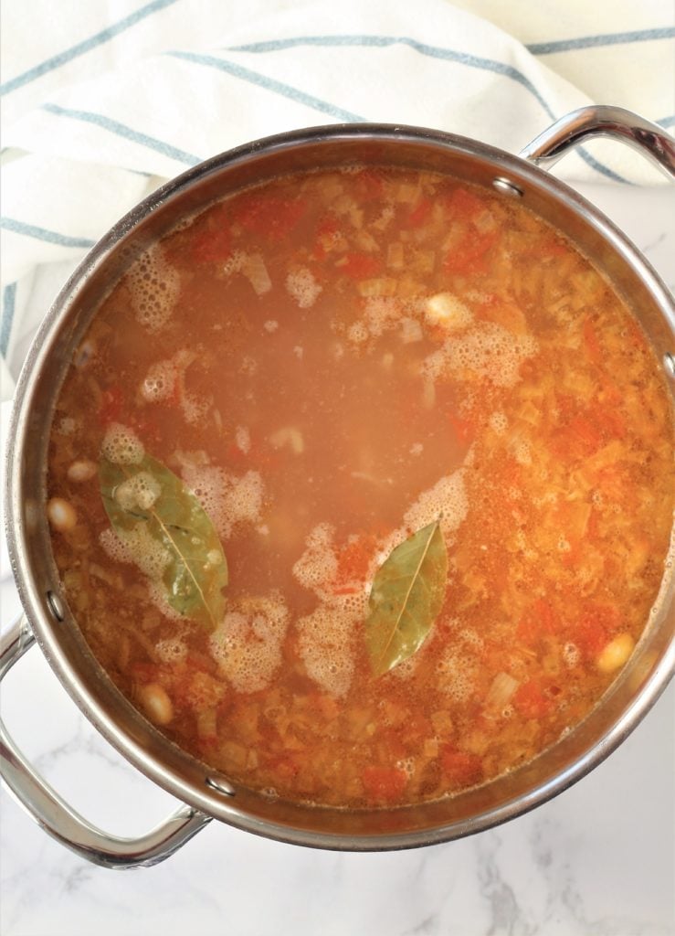 overhead view of stock pot with tomato broth and bay leaves