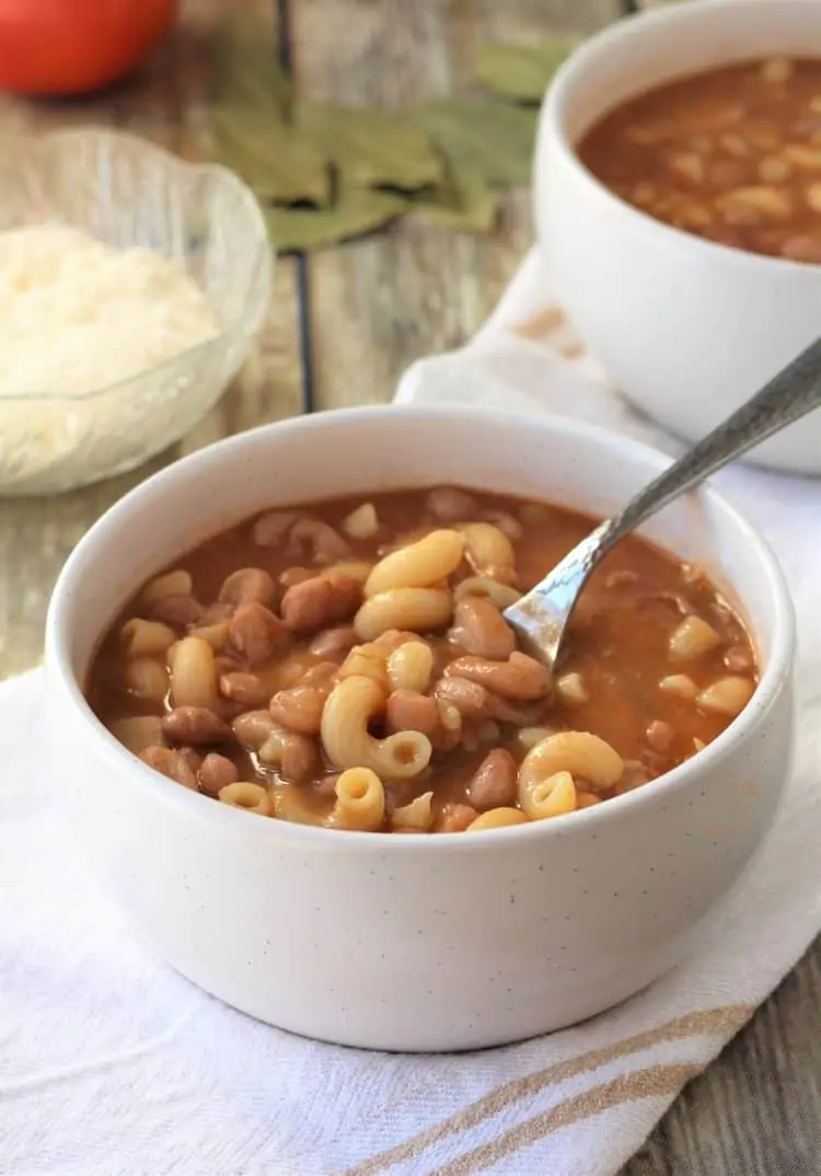 white bowl with pasta and bean soup and spoon submerged in bowl