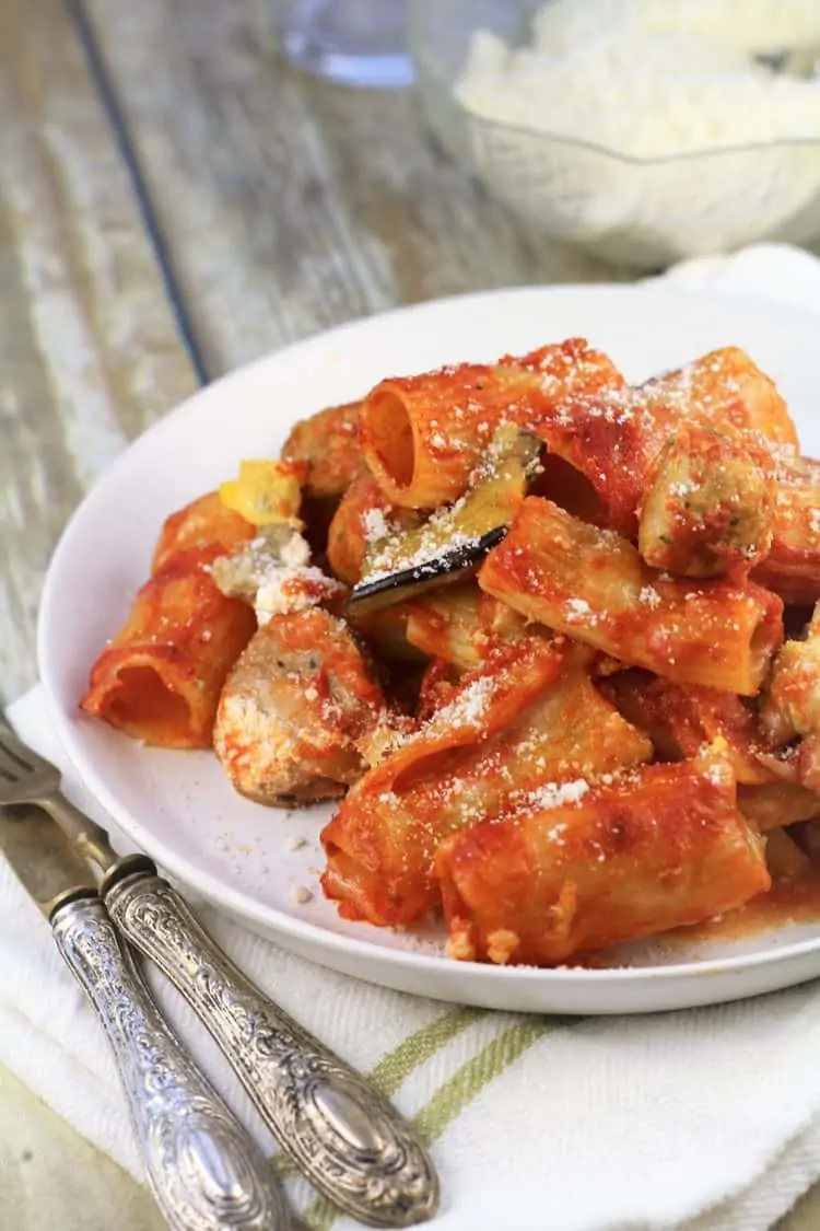 white plate with pasta with tomato sauce topped with grated parmesan