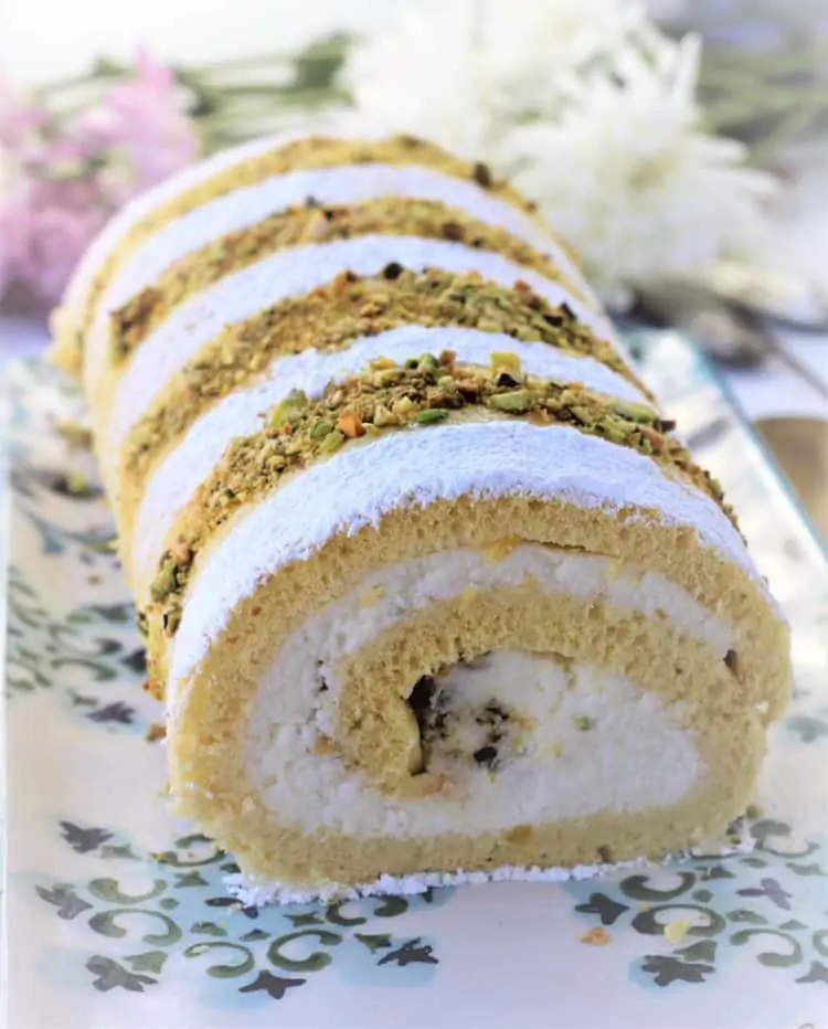 ricotta roll cake on platter topped with powdered sugar and chopped pistachios