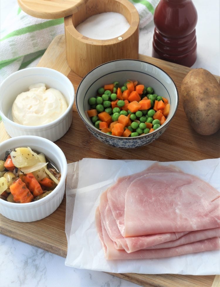 ham slices on white paper, bowl of carrots and peas, bowl of pickled vegetables mayonnaise, potato and salt and pepper 