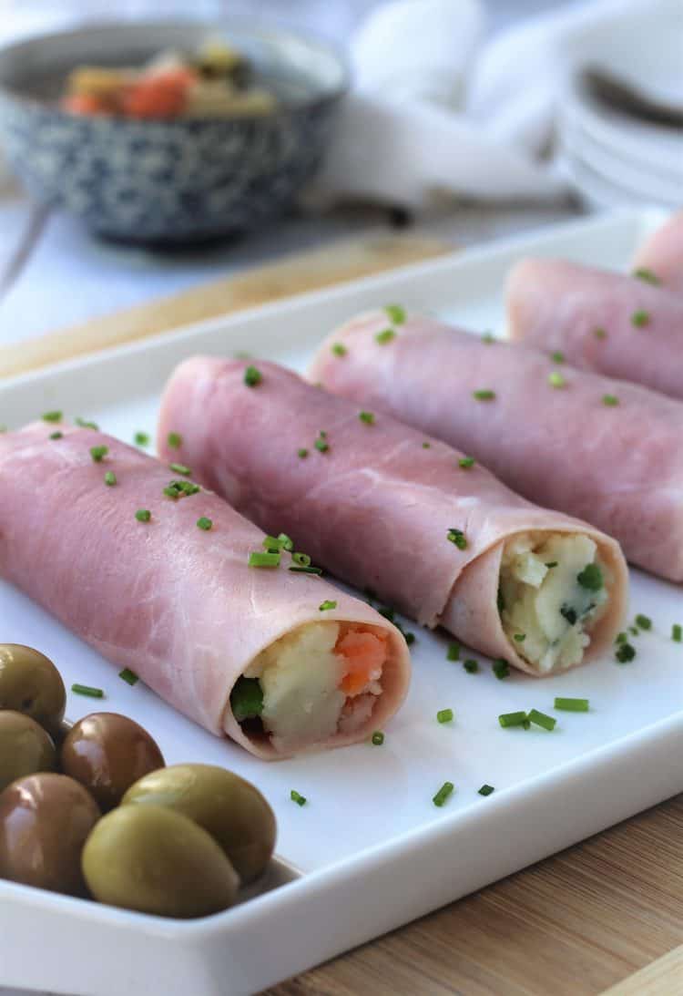 ham rolled around potato salad on white platter with olives 