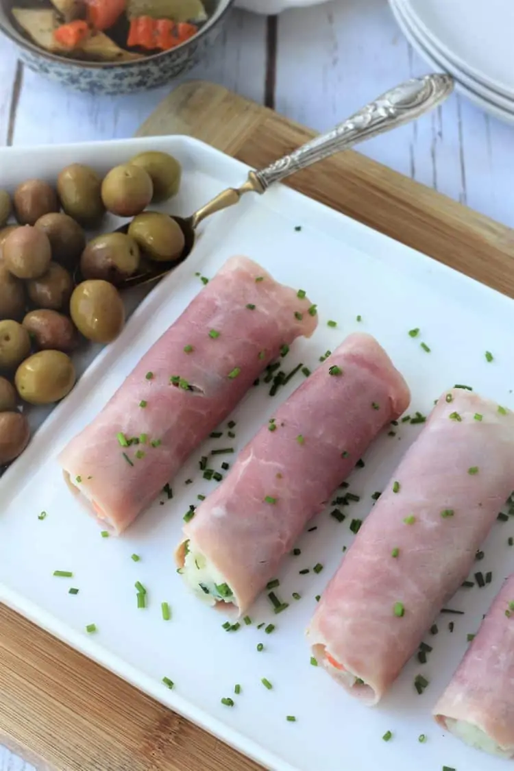 ham rolls on white platter topped with chives and olives on side