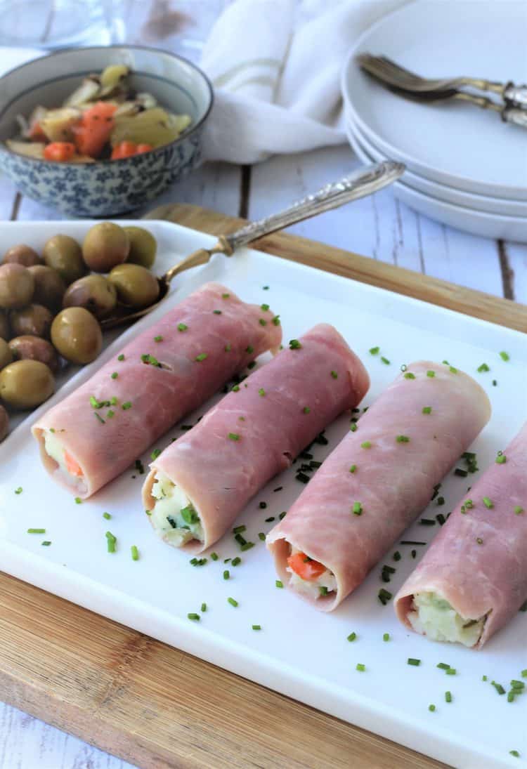 white platter lined with ham rolls with olives on side and plates with forks in background