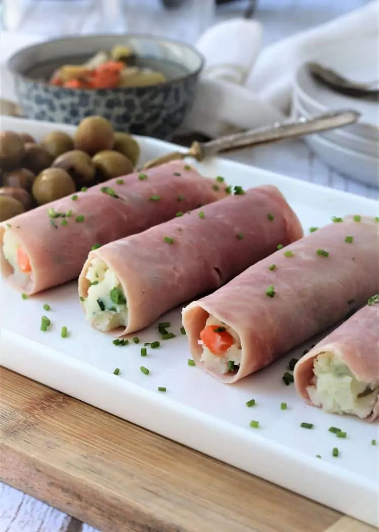 white platter with ham rolls topped with chives and olives on side 
