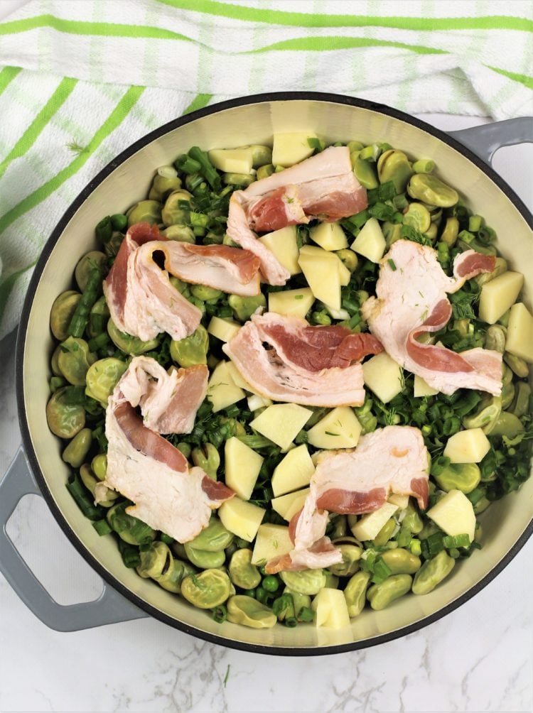 large skillet filled with peas, fava beans, potato and bacon slices 