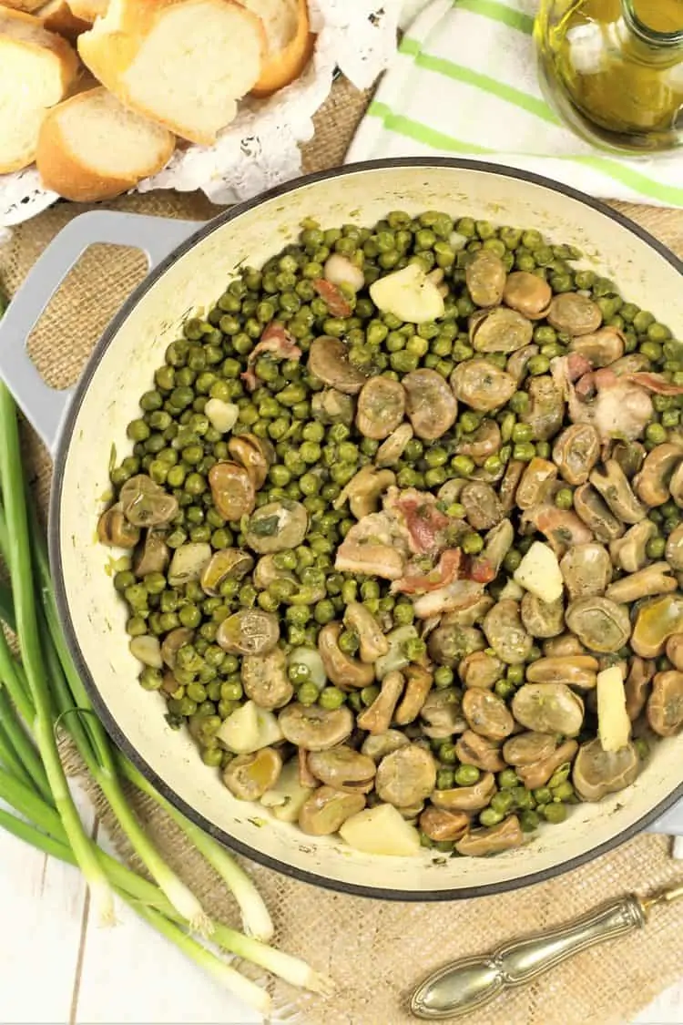 large skillet with fava beans and pea stew surrounded by bread, olive oil and green onions