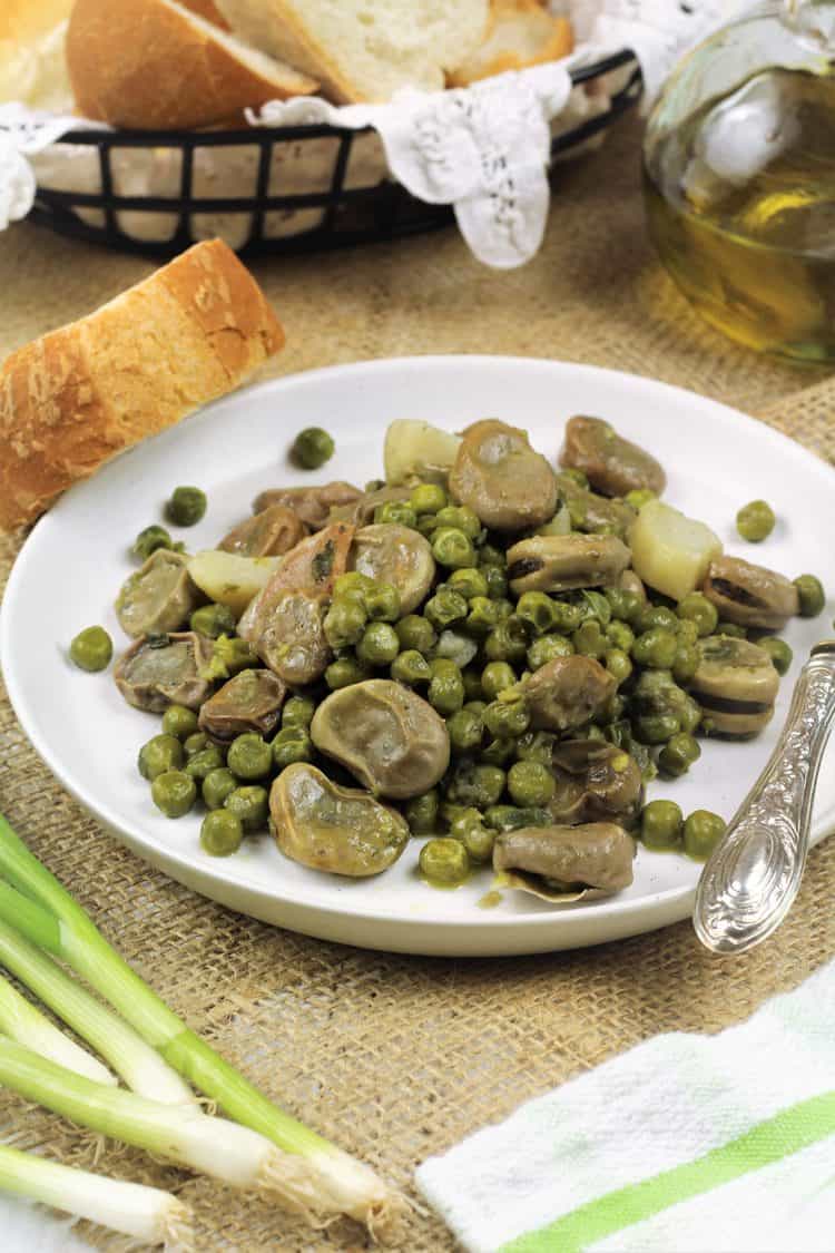 white plate with fava beans and peas with bread on side, green onions and olive oil bottle
